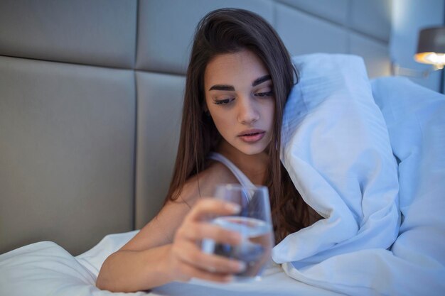 Foto mujer joven bebiendo un vaso de agua en la cama por la noche mujer bebiendo una copa de agua antes de irse a dormir está acostada en la cama