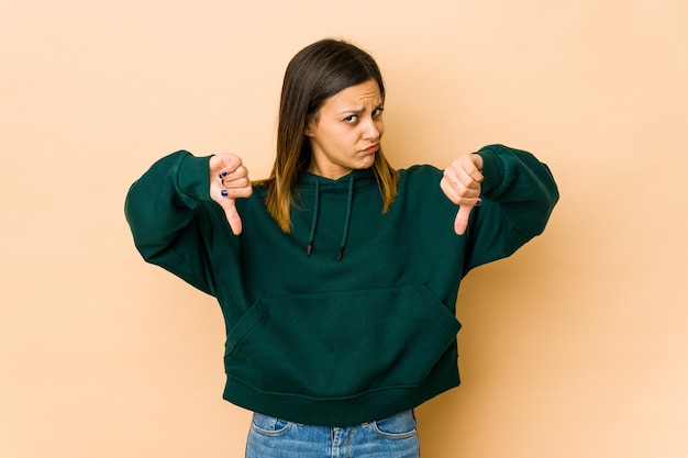 Mujer joven en beige mostrando el pulgar hacia abajo, concepto de decepción.