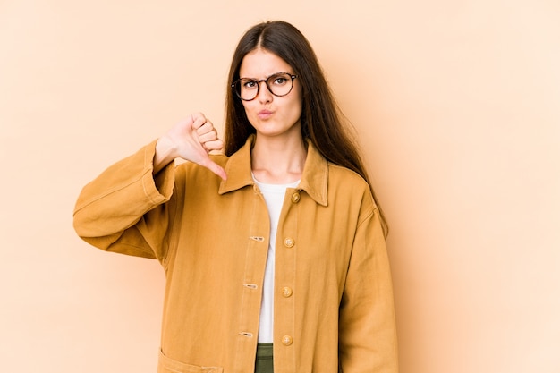 Mujer joven en el beige que muestra el pulgar hacia abajo, concepto de la decepción.