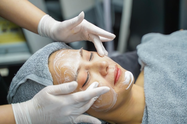 Mujer joven belleza en toalla haciendo masaje facial con exfoliante facial orgánico