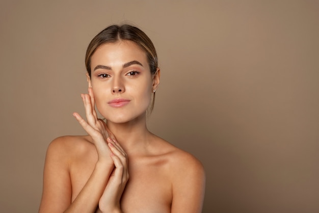 Foto la mujer joven de la belleza toca su rostro con las manos. señora bonita joven con maquillaje natural