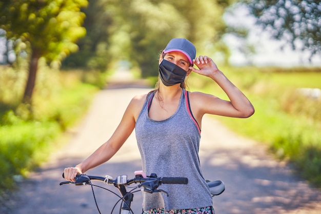 Mujer joven en bicicleta en el campo con una máscara debido a la pandemia de coronavirus