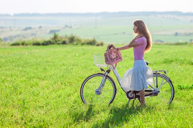 Mujer joven con una bicicleta en campo verde en un día soleado