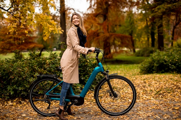 Mujer joven con bicicleta eléctrica en el parque de otoño