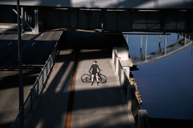 Mujer joven con bicicleta posando al amanecer en el terraplén de la ciudad