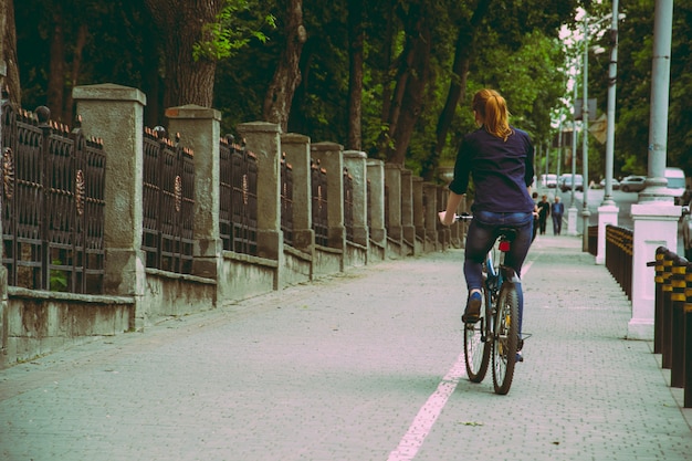 Una mujer joven va en bicicleta hacia la puesta de sol en el parque vintage