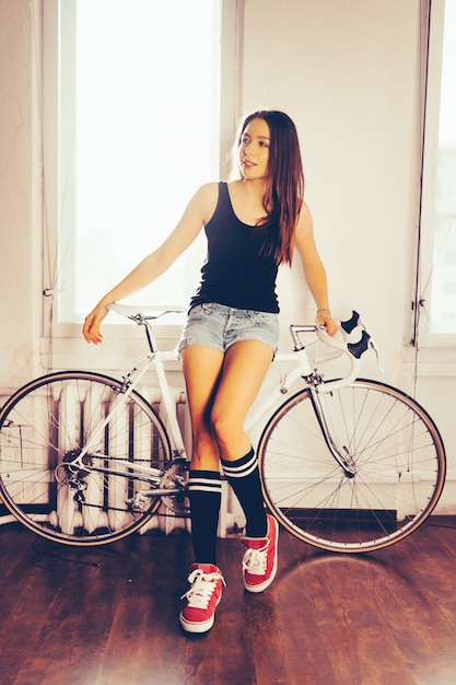 Mujer joven en bicicleta retro blanco, posando en el apartamento interior