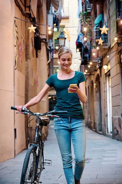 Mujer joven con bicicleta usando su smarphone mientras camina