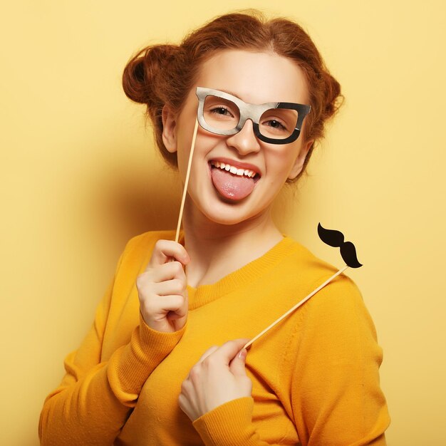 Mujer joven con bigotes falsos y gafas sobre centrico amarillo