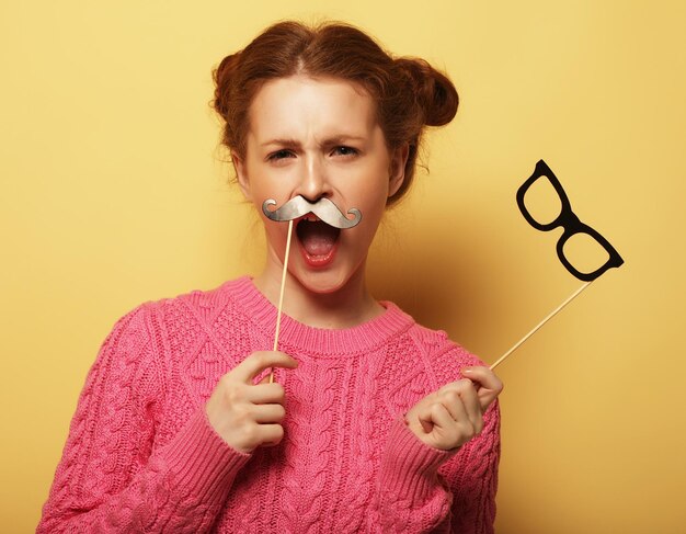 Mujer joven con bigotes falsos y gafas sobre centrico amarillo