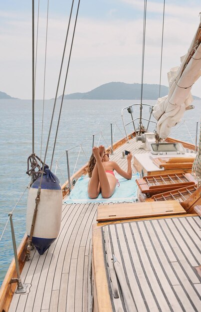 Mujer joven en bikin rojo acostada en un barco tomando el sol tomando fotos con su teléfono celular Mujer disfrutando tomando el sol en un barco durante un crucero tomando selfies con su teléfono celular