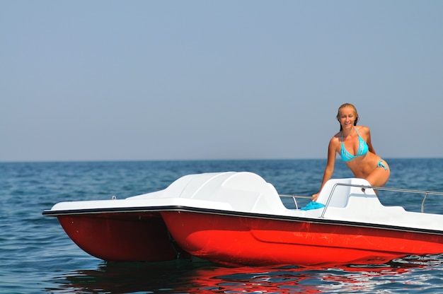 Mujer joven en bikini azul de pie en catamarán blanco