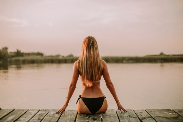 Mujer joven en bikini en el muelle por el río