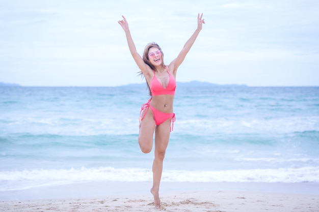 Mujer joven en el bikini que salta en la playa y las ondas de la arena y que se relaja, concepto del viaje del verano.