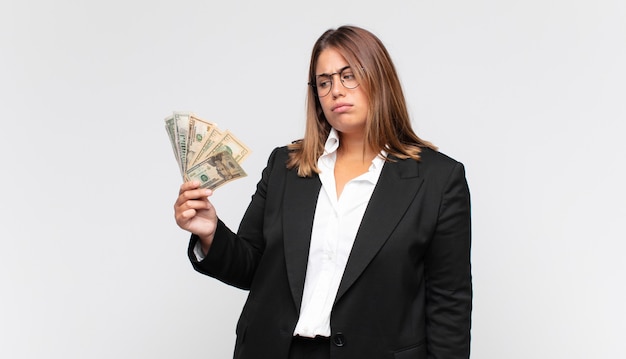 Mujer joven con billetes sintiéndose triste, molesto o enojado y mirando hacia un lado con una actitud negativa, frunciendo el ceño en desacuerdo