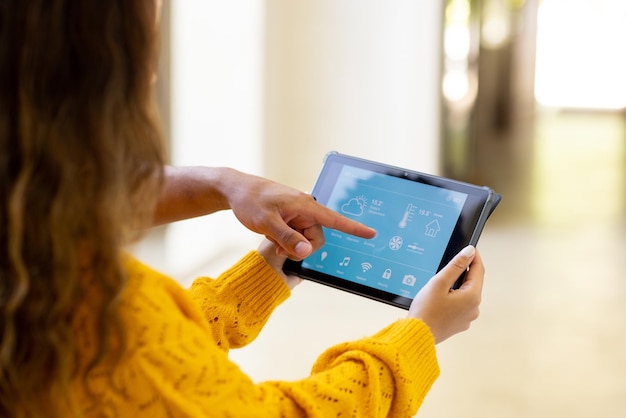 Mujer joven biracial controlando casa inteligente con tableta digital y hombre señalando la aplicación
