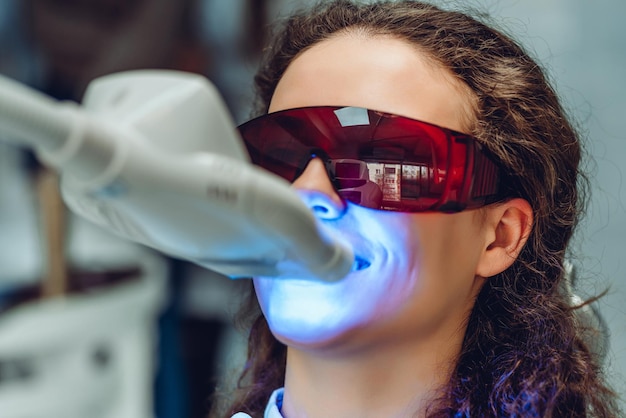 Mujer joven blanquear los dientes en el dentista Vista de cerca