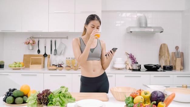 Mujer joven blogger asiática con smartphone para hablar, chatear y consultar las redes sociales en la cocina