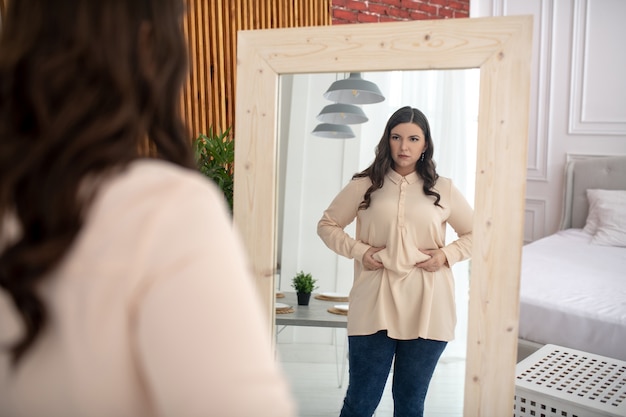 Mujer joven en una blusa beige tocando su vientre