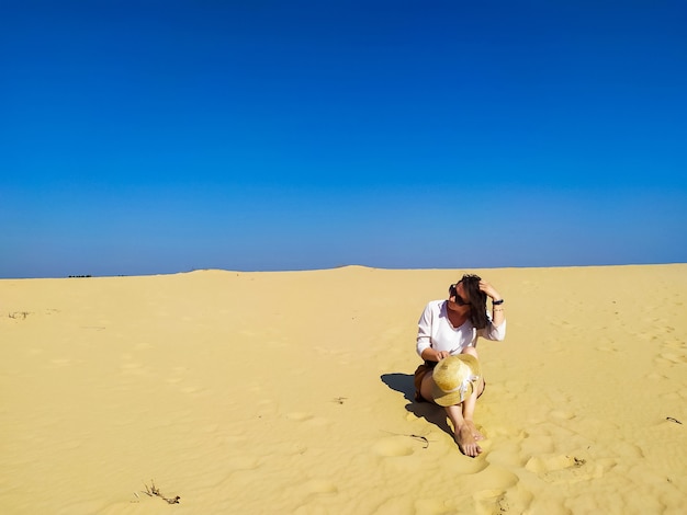 Mujer joven en blusa blanca y pantalones cortos marrones caminando en el desierto