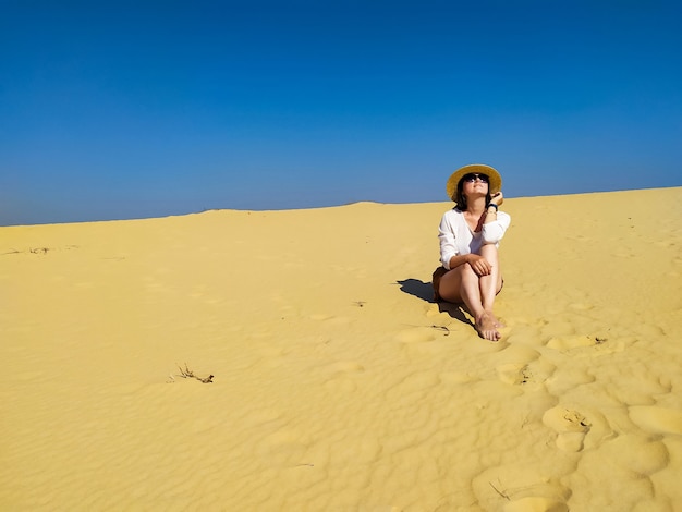 Mujer joven en blusa blanca y pantalones cortos marrones caminando en el desierto