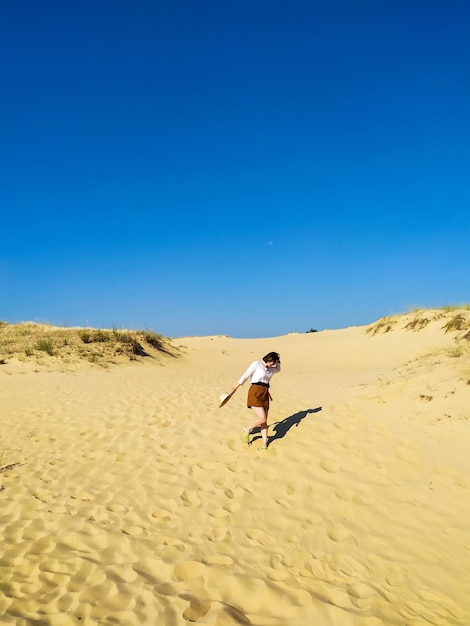 Mujer joven en blusa blanca y pantalones cortos marrones caminando en el desierto