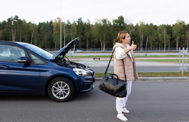 Una mujer joven con una bolsa al hombro vota en la carretera y busca un paseo junto a un derrumbado