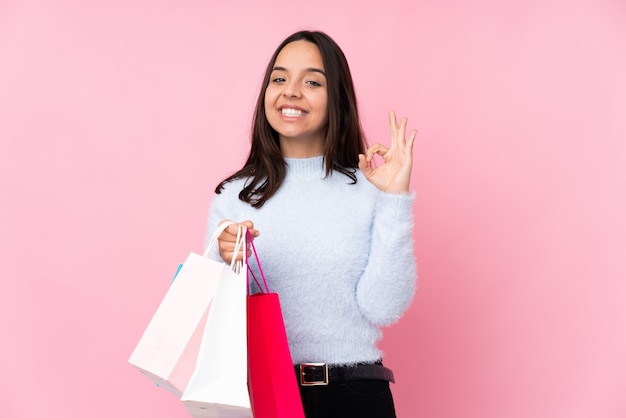 Foto mujer joven con bolsa de compras sobre la pared de color rosa que muestra bien firmar con los dedos