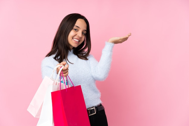 Mujer joven con bolsa de compras sobre pared rosa aislada extendiendo las manos hacia el lado para invitar a venir