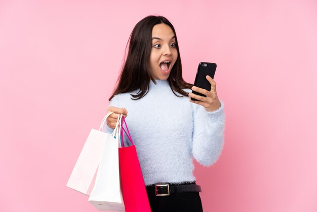 Foto mujer joven con bolsa de compras sobre pared rosa aislado con café para llevar y un móvil