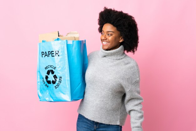 Mujer joven con una bolsa de reciclaje aislada en coloridos mirando hacia el lado y sonriendo