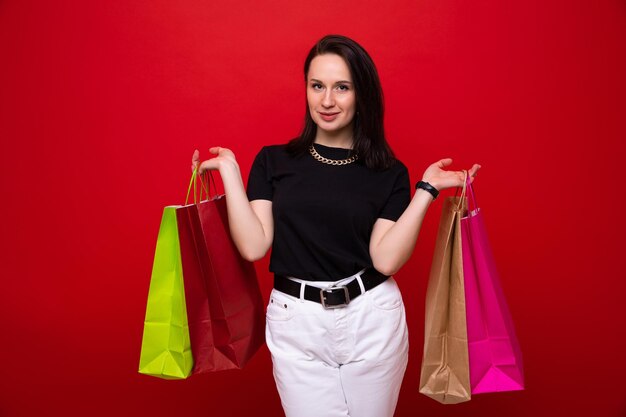 Una mujer joven con bolsas de colores sobre un fondo rojo.