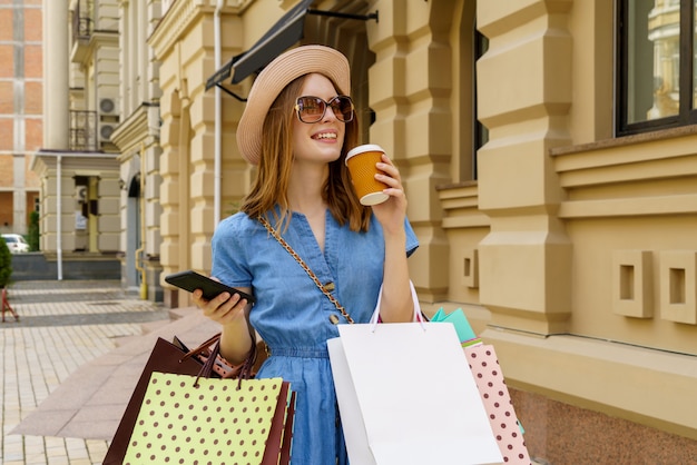 Mujer joven con bolsas de compras caminando en una ciudad en verano