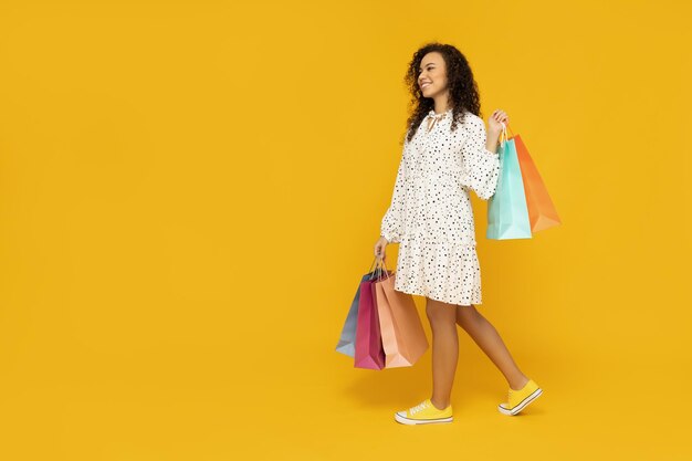 Mujer joven con bolsas de compras sobre fondo amarillo