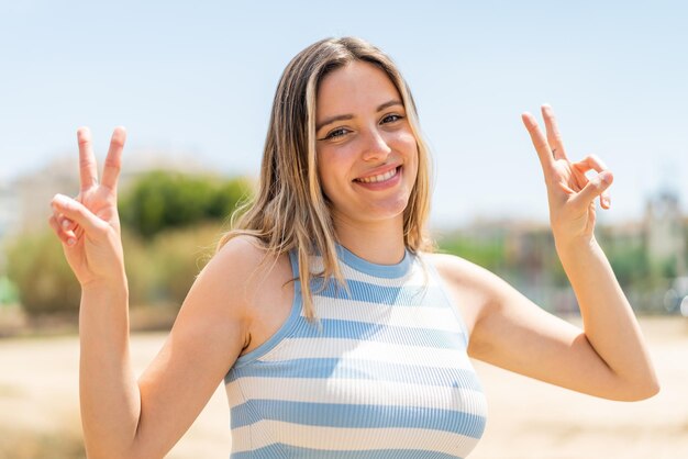 Foto mujer joven y bonita al aire libre mostrando el signo de la victoria con ambas manos