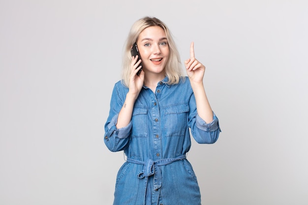 Mujer joven bonita albina que se siente como un genio feliz y emocionado después de darse cuenta de una idea y hablar con un teléfono inteligente