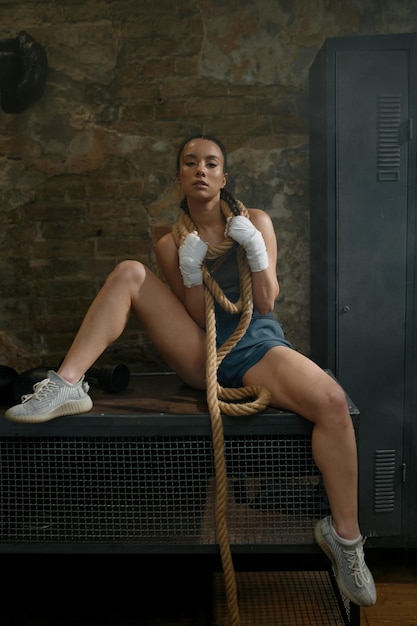 Mujer joven y bonita boxeadora envuelta en una cuerda de arrastre sobre el cuello retrato atmosférico. Modelo de kickboxer femenino de glamour. Concepto deportivo de boxeo