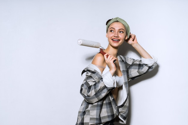 Una mujer joven y bonita con una camisa pinta las paredes con un rodillo en su nuevo apartamento