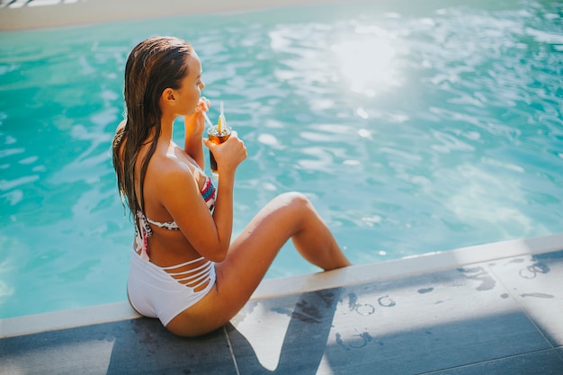 Mujer joven y bonita junto a la piscina con un cóctel