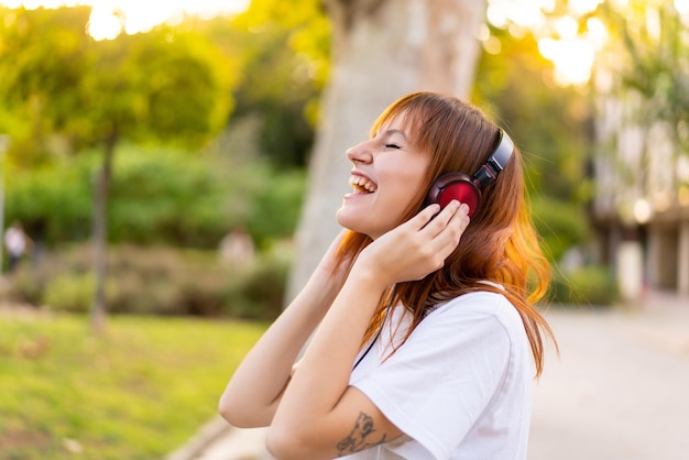 Mujer joven bonita pelirroja al aire libre escuchando música y cantando