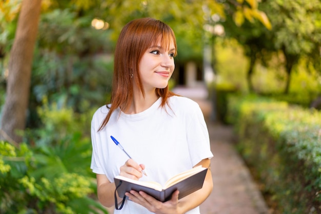 Mujer joven bonita pelirroja al aire libre sosteniendo un cuaderno