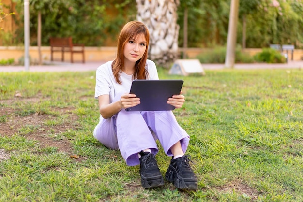 Mujer joven bonita pelirroja al aire libre sosteniendo una tableta
