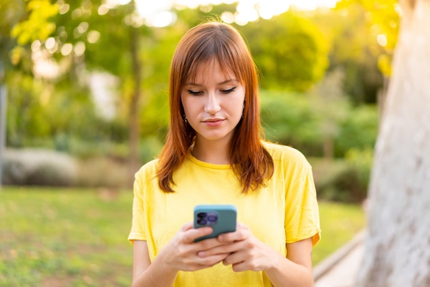 Mujer joven bonita pelirroja al aire libre mediante teléfono móvil