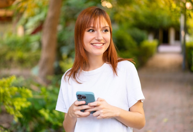 Mujer joven bonita pelirroja al aire libre mediante teléfono móvil