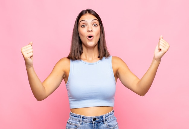 Foto una mujer joven y bonita que celebra un éxito increíble como una ganadora, se ve emocionada y feliz y dice ¡toma eso!