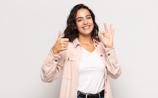 Mujer joven y bonita que se siente feliz, asombrada, satisfecha y sorprendida, mostrando gestos de aprobación y pulgar hacia arriba, sonriendo