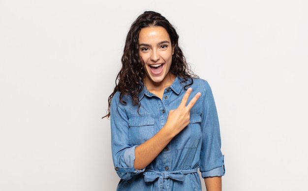 Mujer joven y bonita que se siente feliz, positiva y exitosa, con la mano haciendo forma de v sobre el pecho, mostrando la victoria o la paz