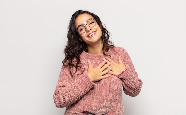 Mujer joven y bonita que se siente romántica, feliz y enamorada, sonriendo alegremente y tomados de la mano cerca del corazón