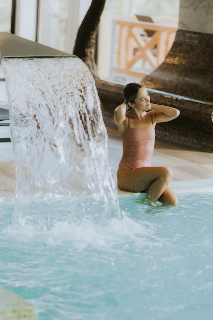 Mujer joven y bonita relajándose junto a la piscina cubierta