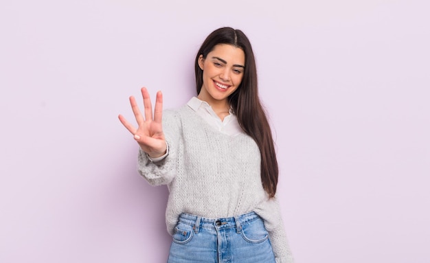 mujer joven y bonita sonriendo y luciendo amistosa, mostrando el número cuatro o cuarto con la mano hacia adelante, contando hacia atrás